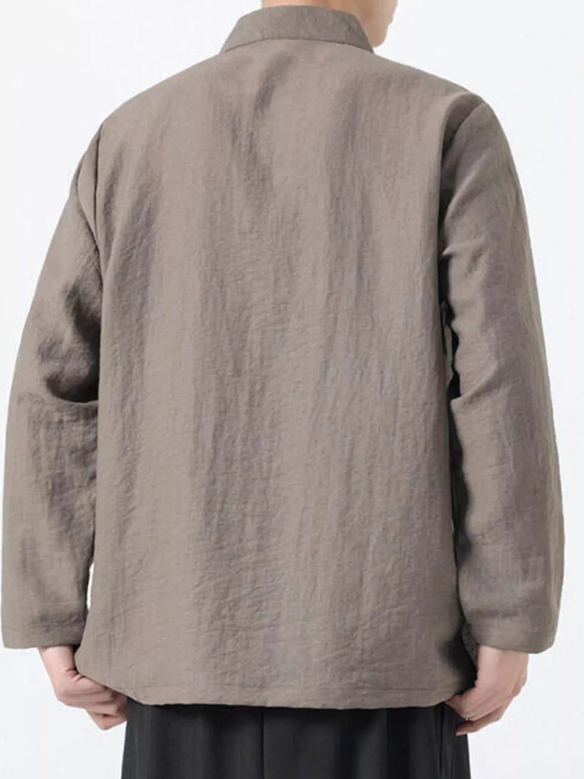 A person shown from the back wearing a loose, long-sleeve linen jacket in a taupe-brown color, paired with black trousers, against a plain white background.