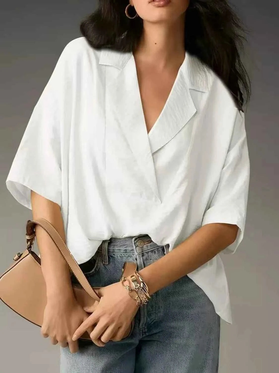 Person wearing a white blouse and holding a beige handbag against a gray background