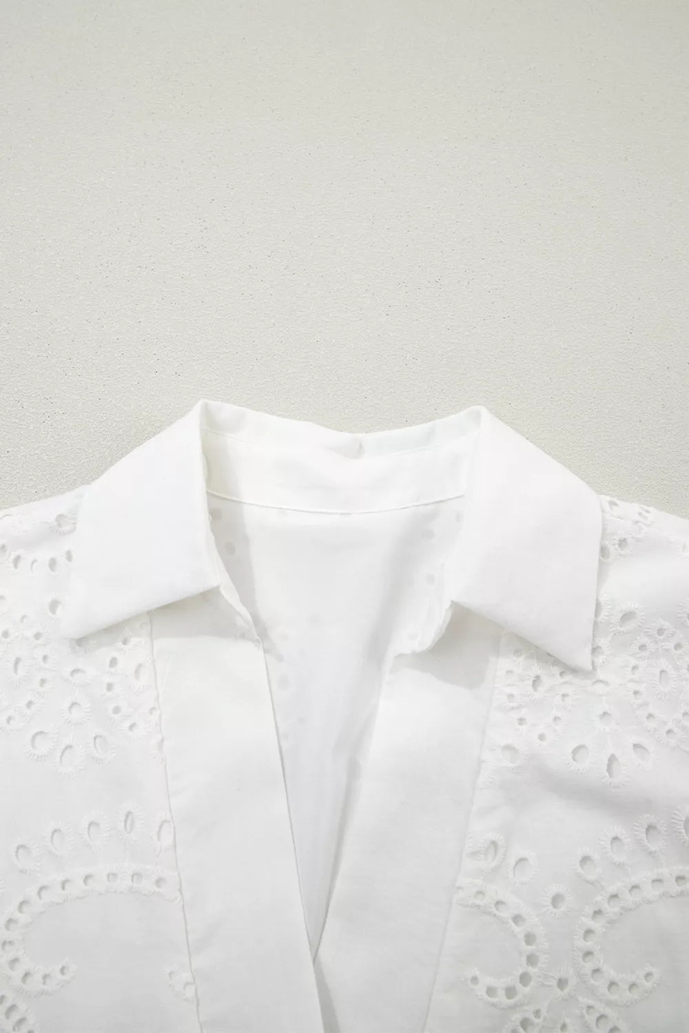 White blouse with intricate cut-out detailing on a light gray background