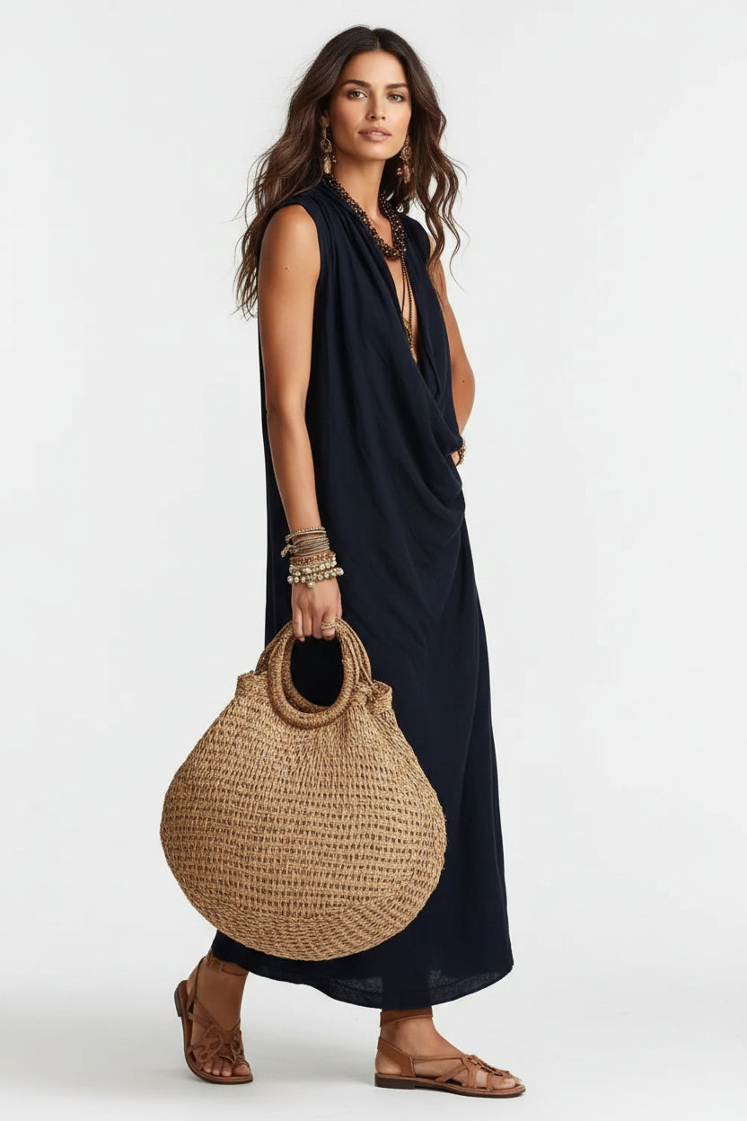 Woman in a black sleeveless dress holding a woven bag against a neutral background