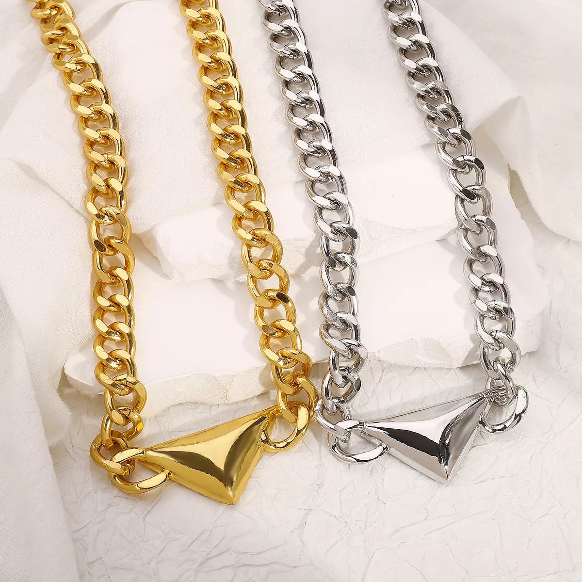 Two chain necklaces, one gold and one silver, on a textured white surface.