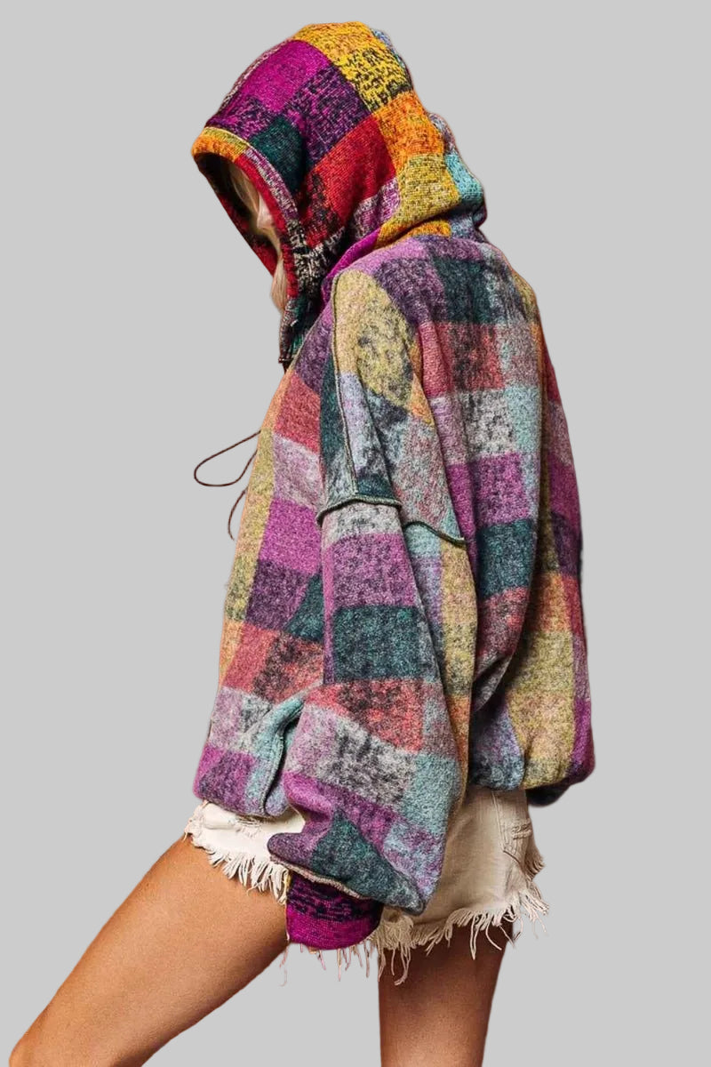 Person wearing a colorful hooded blanket against a brown wall