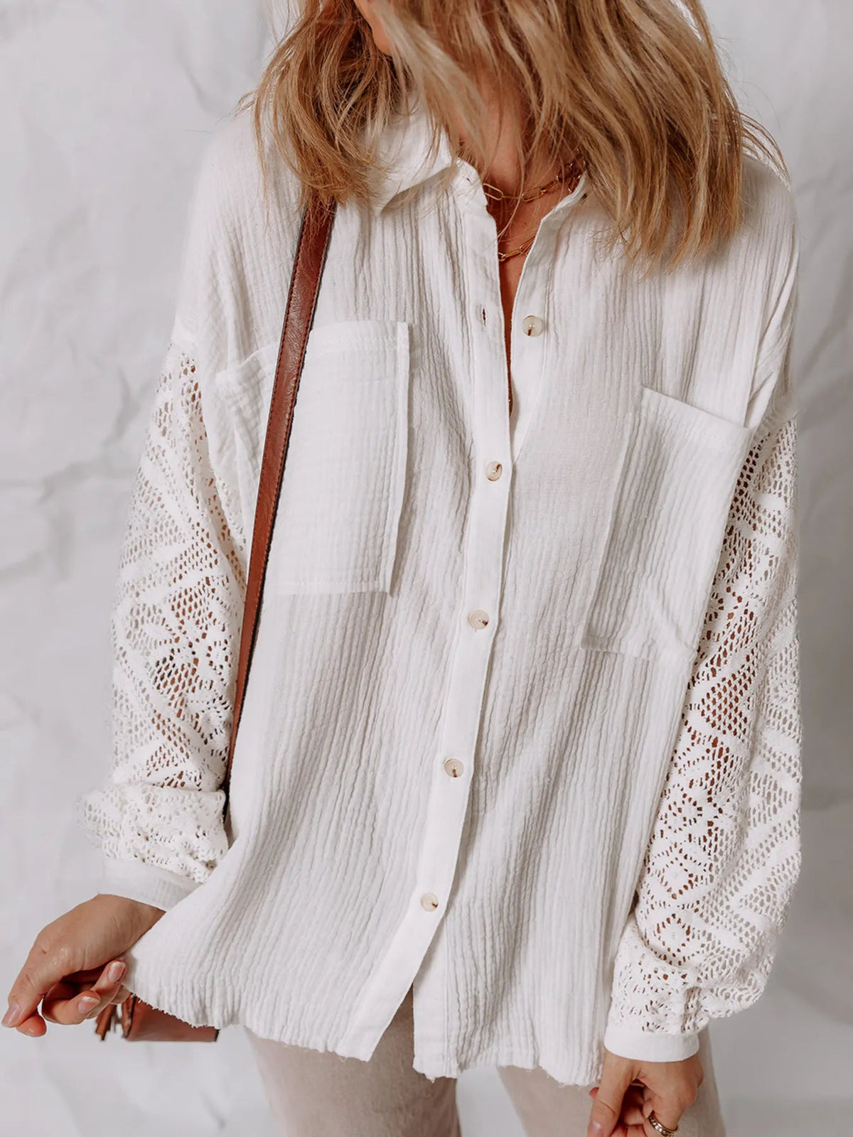 A woman wearing a white long-sleeve button-up shirt with textured crinkle fabric and intricate lace crochet detailing on the sleeves, styled with a brown shoulder bag.