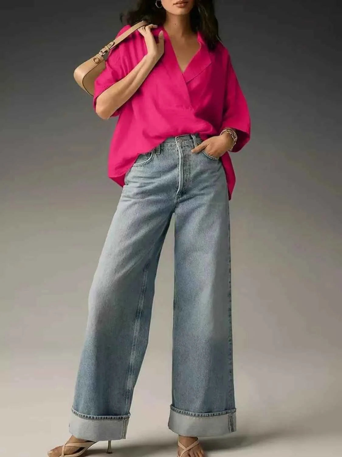 Woman wearing a bright pink blouse and light blue jeans against a neutral background