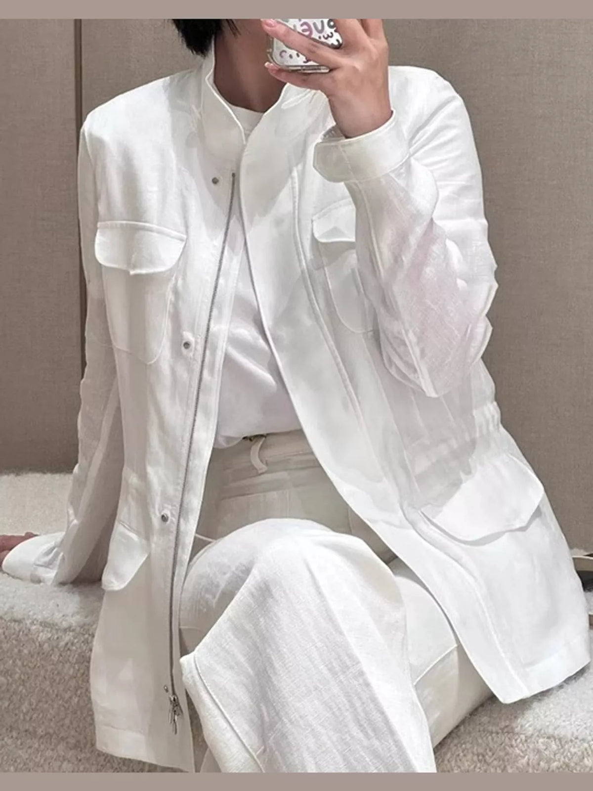 Woman wearing a white long-sleeve linen utility jacket with front flap pockets and matching white pants against a neutral studio background.