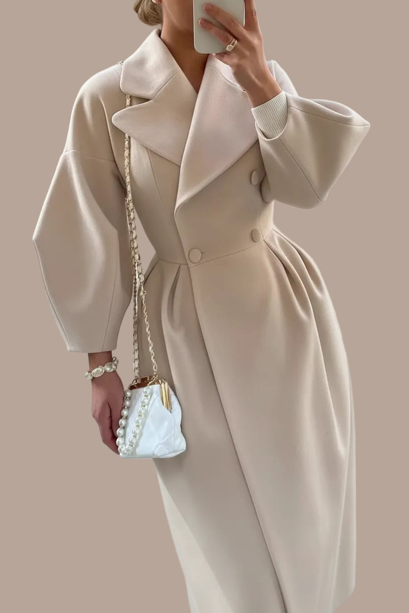 Person wearing a long beige coat holding a white handbag with pearls on a paved street.