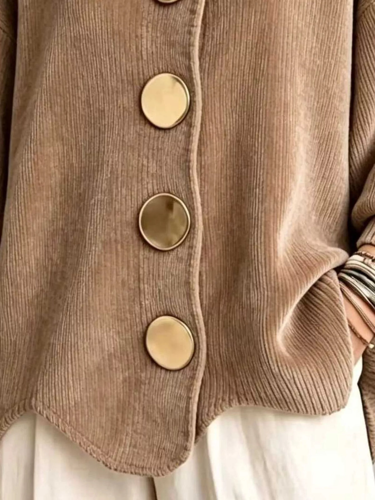 Close-up of a taupe corduroy cardigan with large round gold-tone buttons, worn over white bottoms.