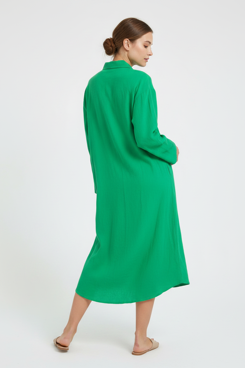 A woman wearing a bright green long-sleeve midi shirt dress, shown from a side-back angle against a plain white studio background.