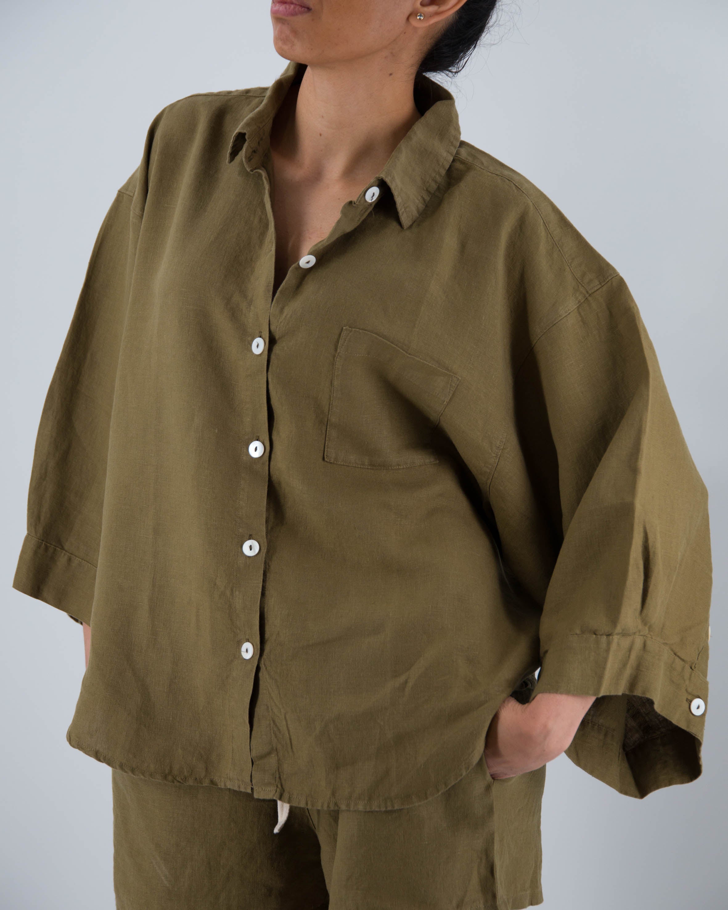 Person wearing a brown shirt with rolled-up sleeves on a plain background