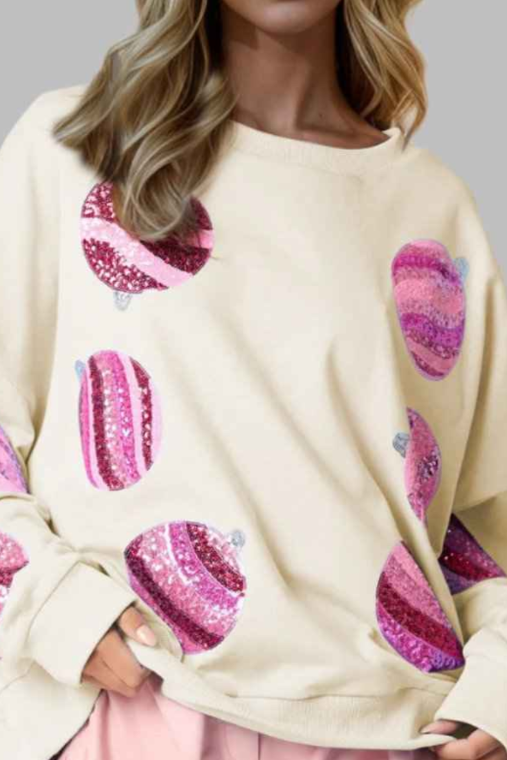 Woman wearing a cream sweater with pink heart patterns and pink shorts on a gray background