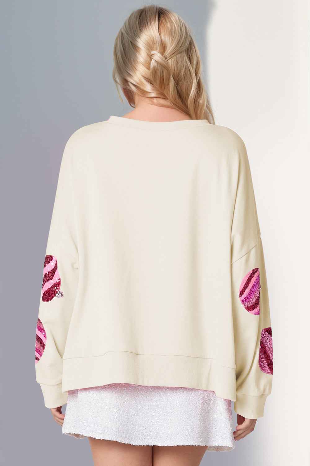 Beige sweater with pink designs on sleeves worn by a person against a gray background