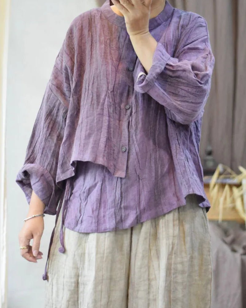 Person wearing a loose-fitting, long-sleeve purple shirt with a neutral background