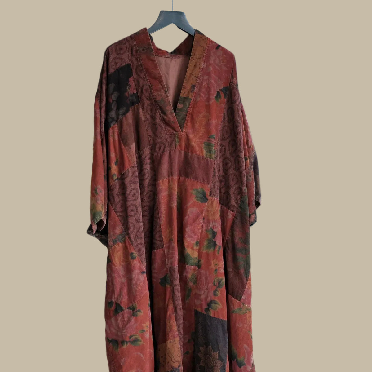 Long, patterned dress hanging on a mannequin in a room with plants and furniture.