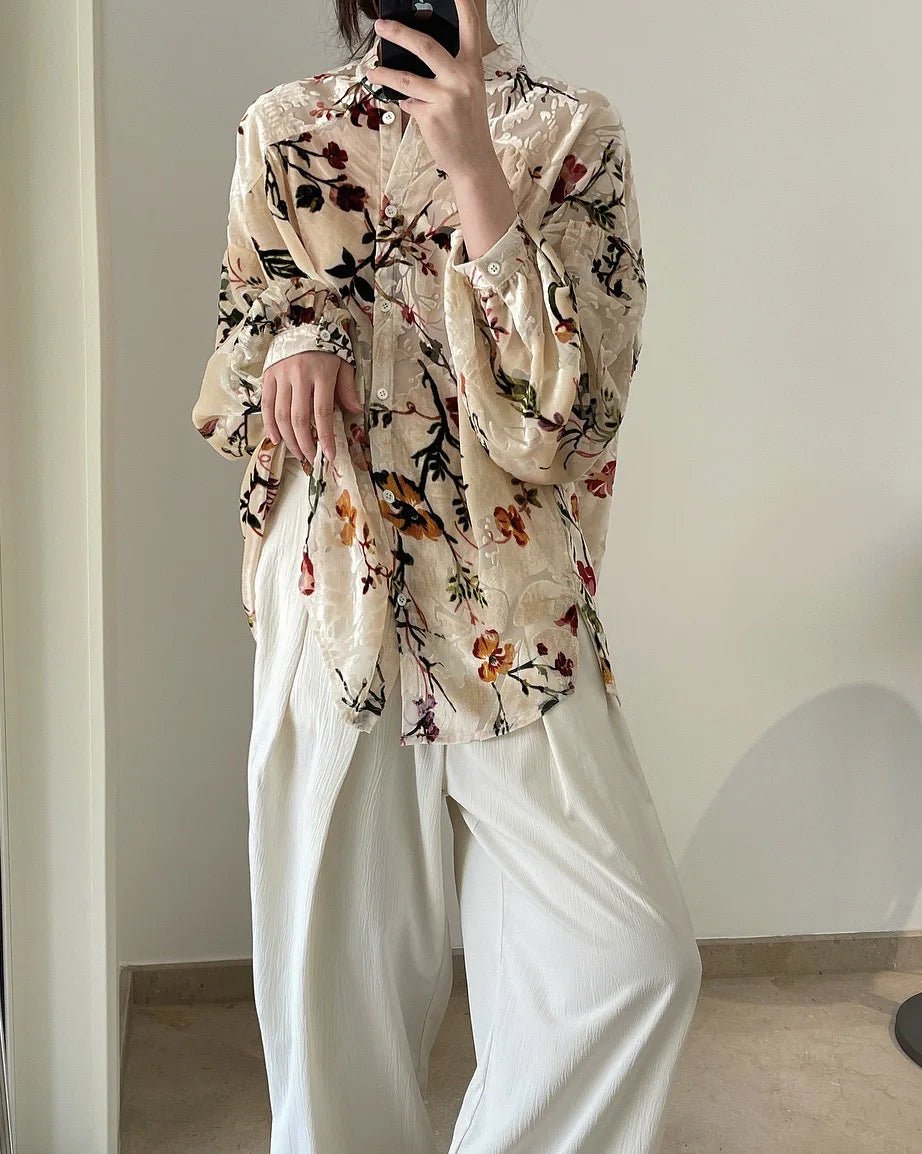 Person wearing a floral blouse and white pants in a minimal indoor setting