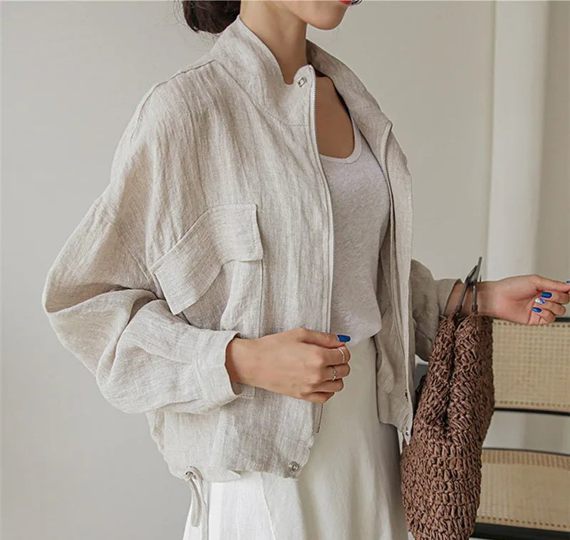 Person wearing a light-colored jacket holding a woven bag indoors.