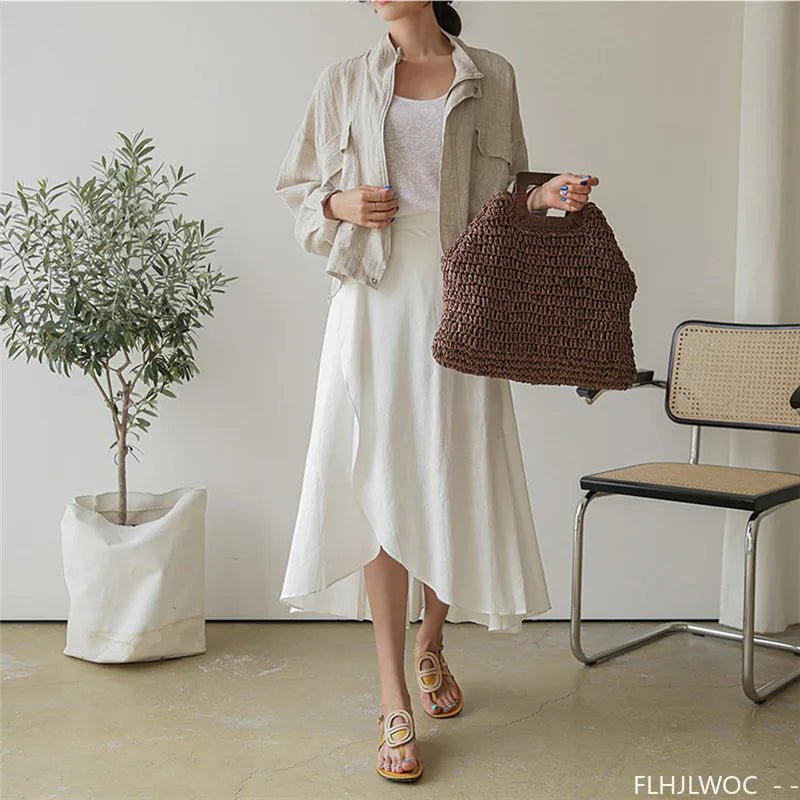 Woman holding a brown woven bag in a minimalistic room with a plant and chair.