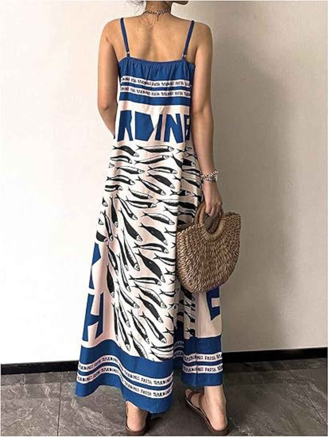 Woman wearing a blue and white patterned dress holding a straw bag indoors.