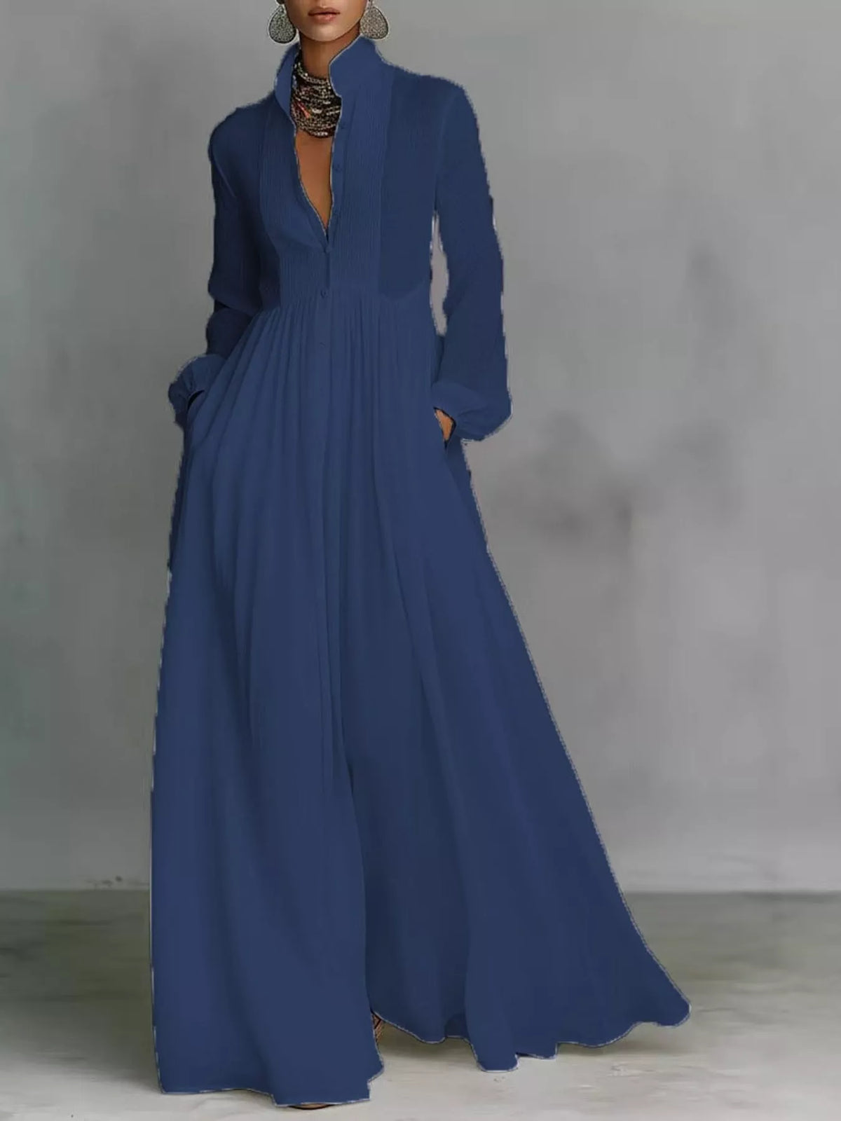 A woman wearing a long-sleeve, high-neck maxi dress in a solid medium blue, standing against a textured gray studio background.