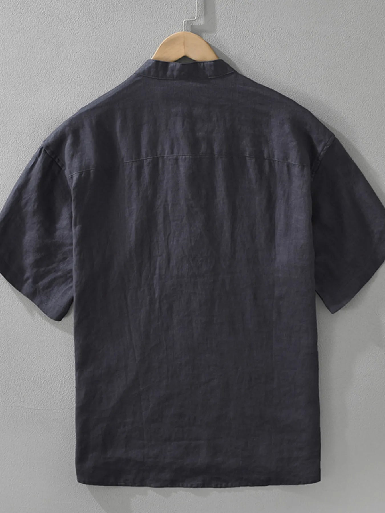 Black short-sleeve shirt on a hanger against a gray wall