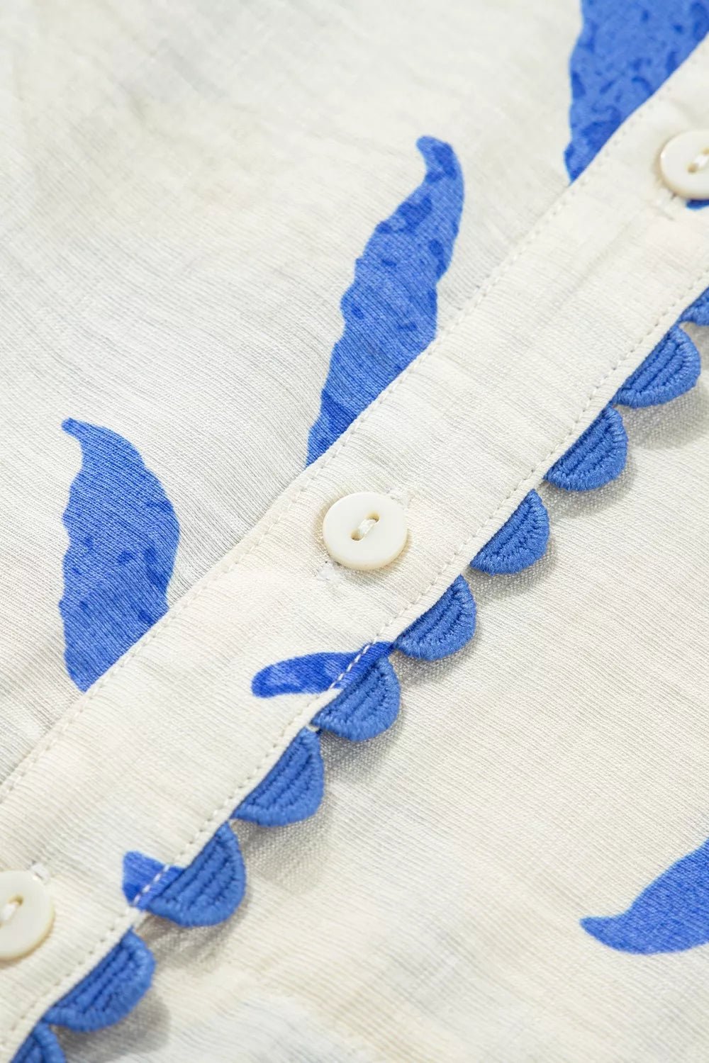 Close-up of a white garment with blue leaf patterns and buttons.