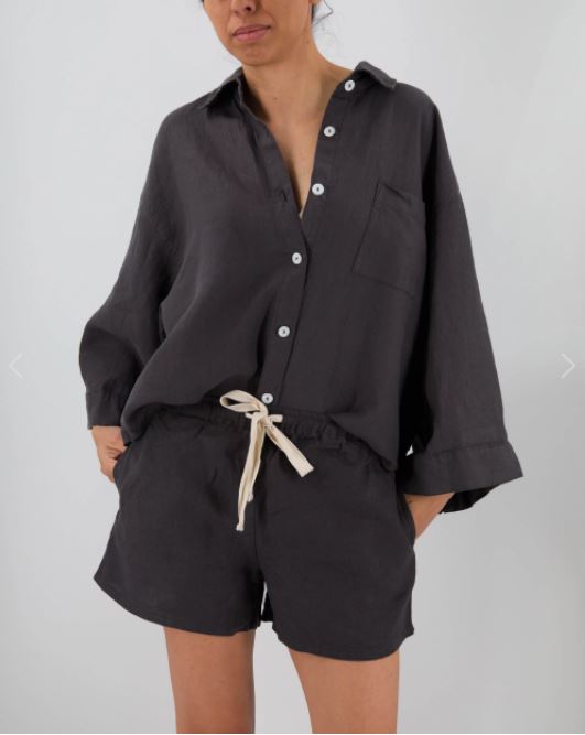 Person wearing a black button-up shirt and shorts on a plain background