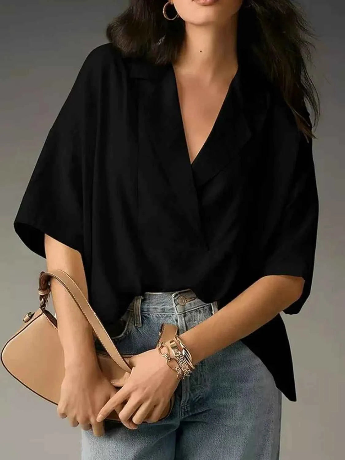 Person wearing a black top and holding a beige handbag against a neutral background