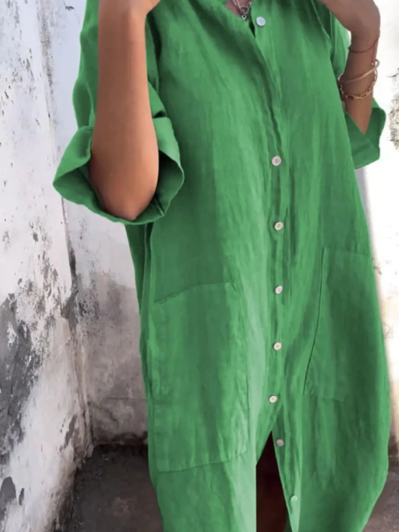 Person wearing a green dress with button details against a textured wall.