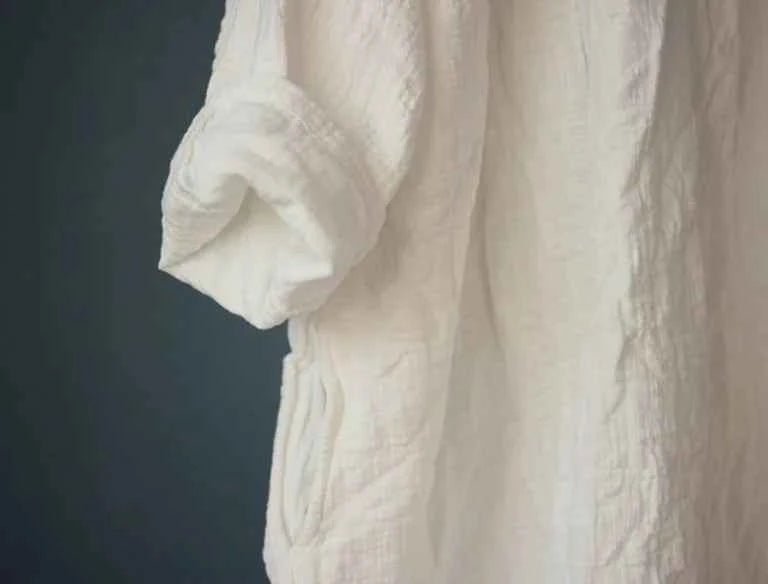 A close-up of a textured off-white or cream crinkled fabric garment, showing the rolled-up sleeve and body, set against a dark slate gray background.