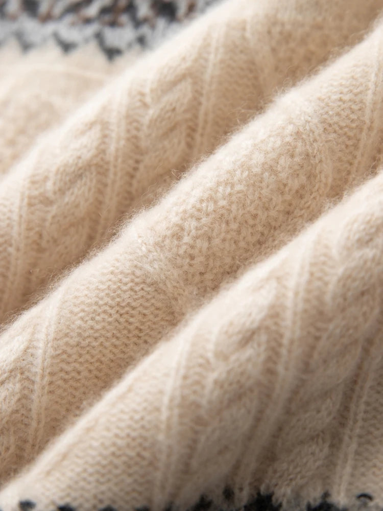 Close-up of a cream-colored cable-knit fabric with soft folds and a hint of a dark patterned textile at the top edge.