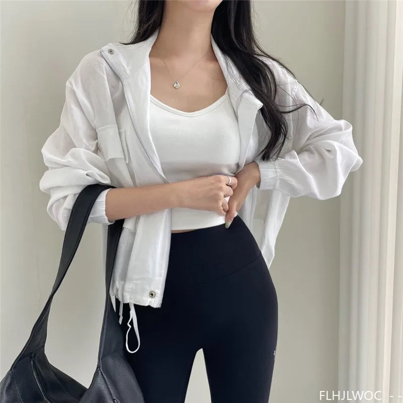 Person wearing a white jacket, white top, and black leggings holding a black bag indoors.