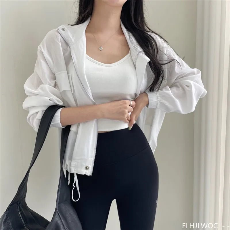 Person wearing a white jacket, white top, and black leggings holding a black bag indoors.