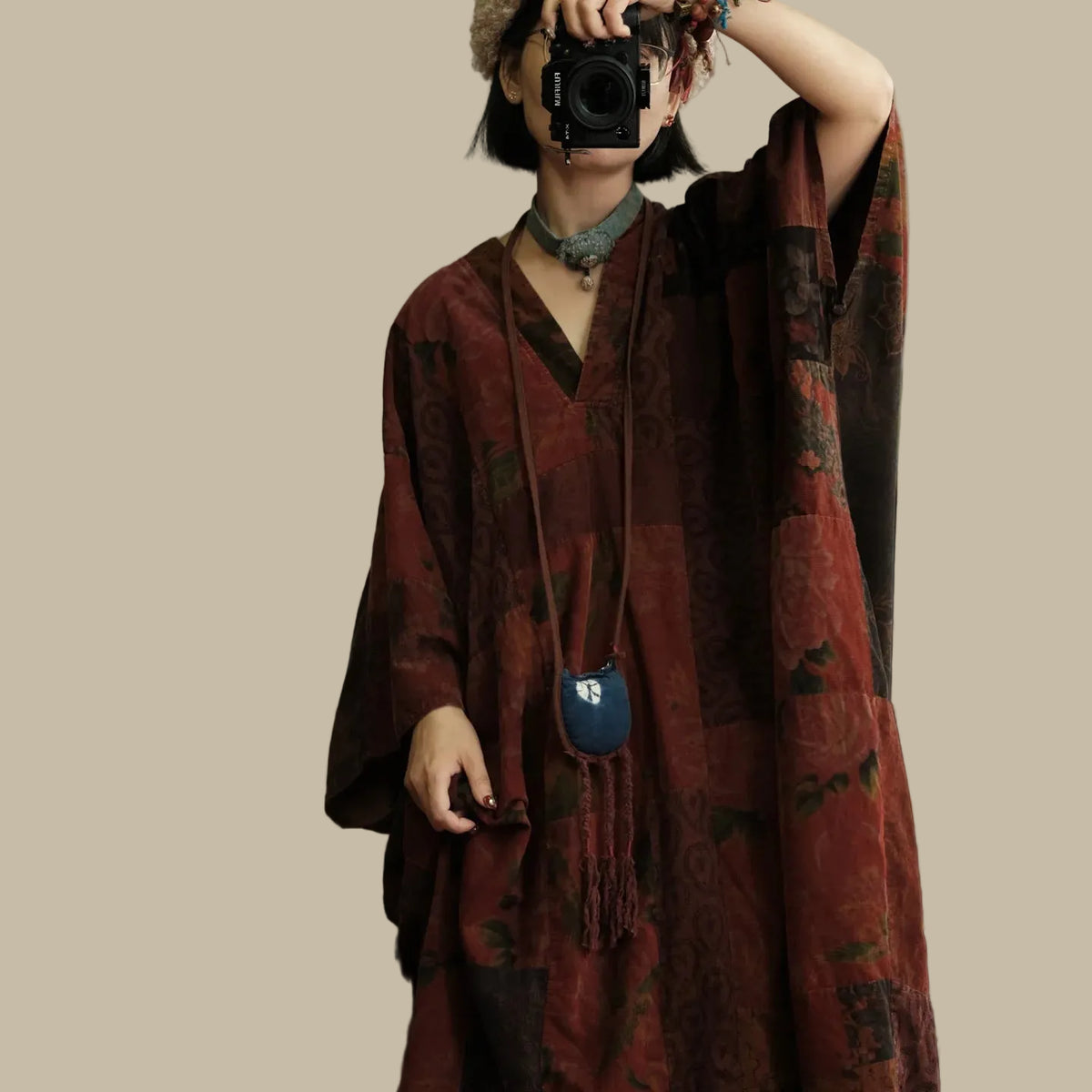 Person wearing a patterned dress holding a camera, with a blurred indoor background