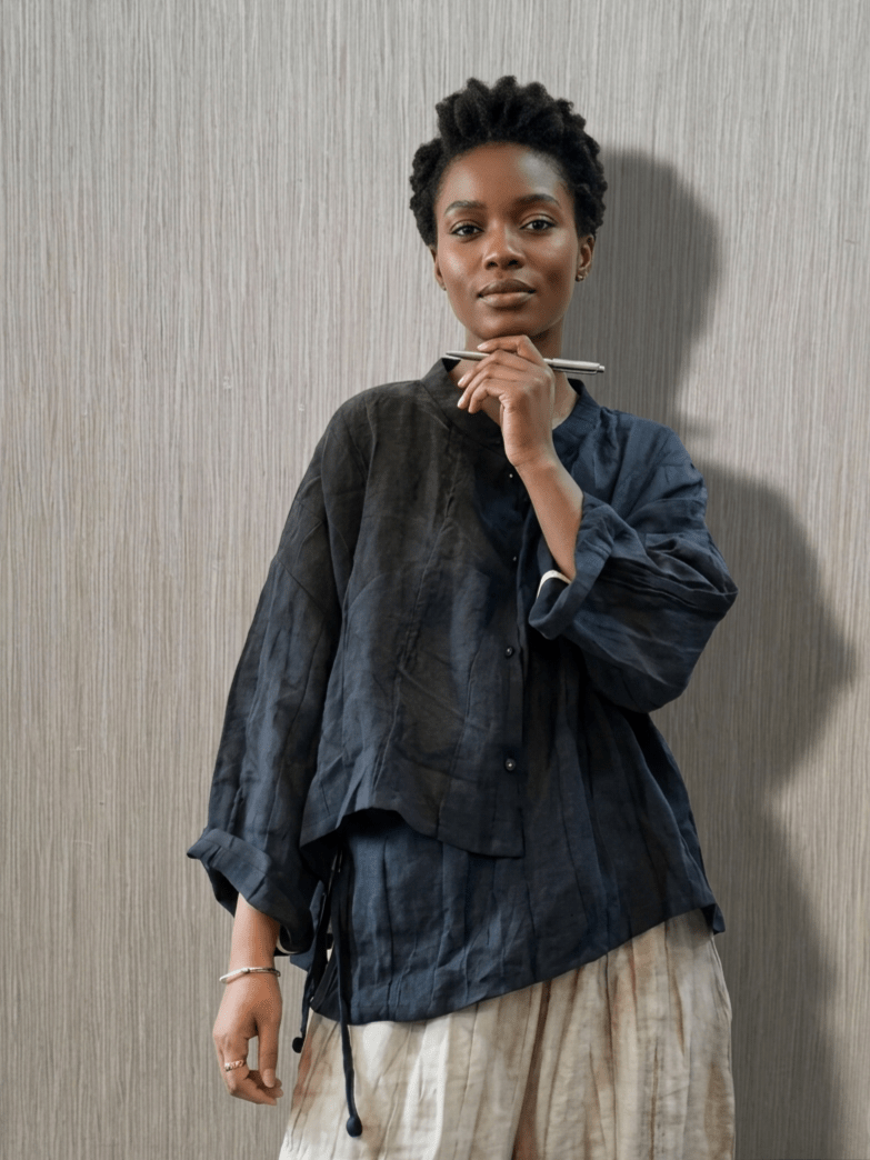 Woman wearing a dark blue shirt and light-colored pants against a neutral background