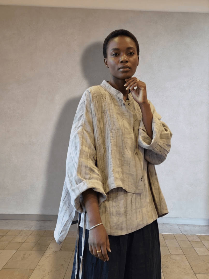 Person wearing a beige layered shirt against a plain wall.