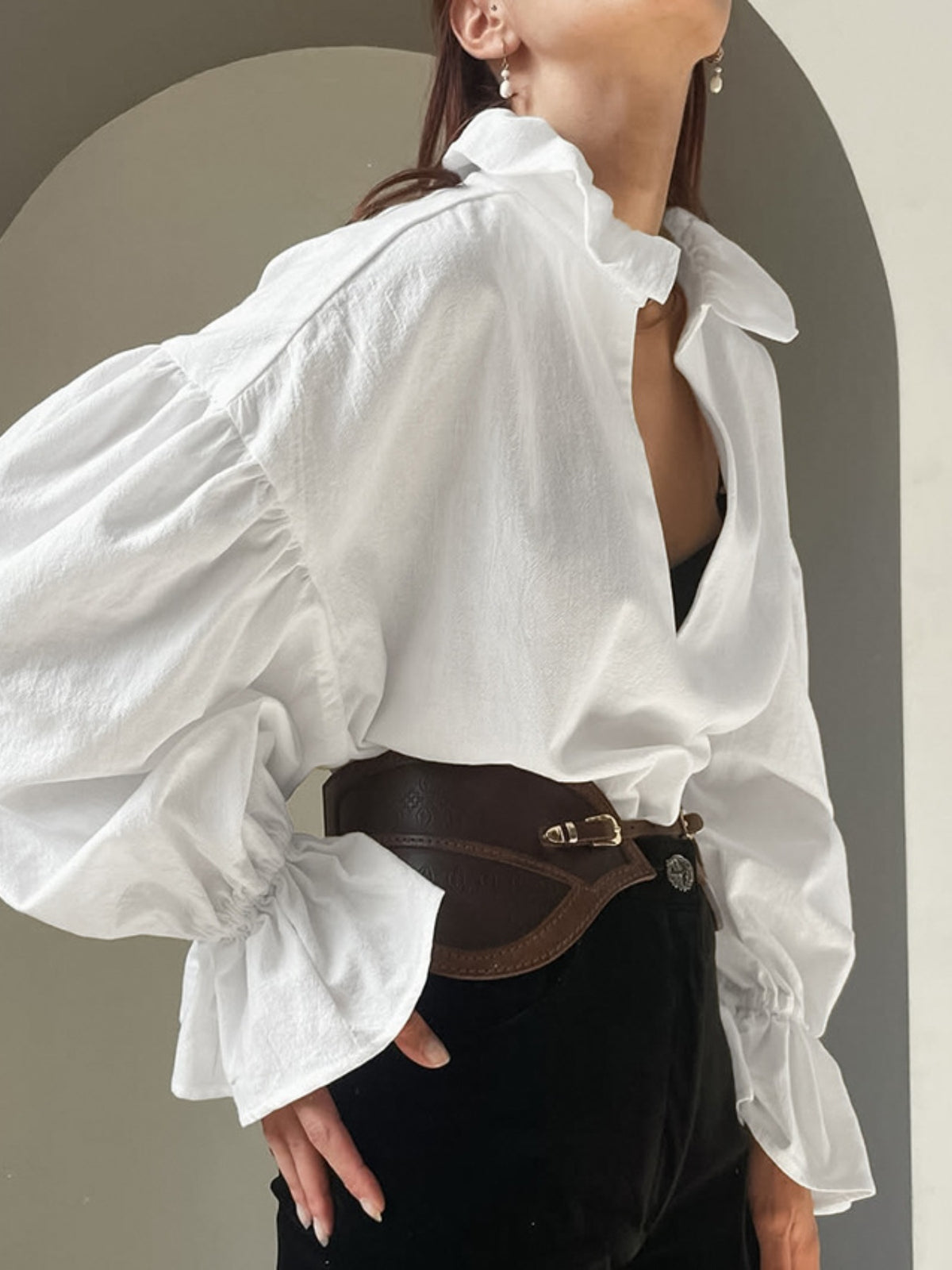 Person wearing a white oversized shirt with a brown belt against a neutral background