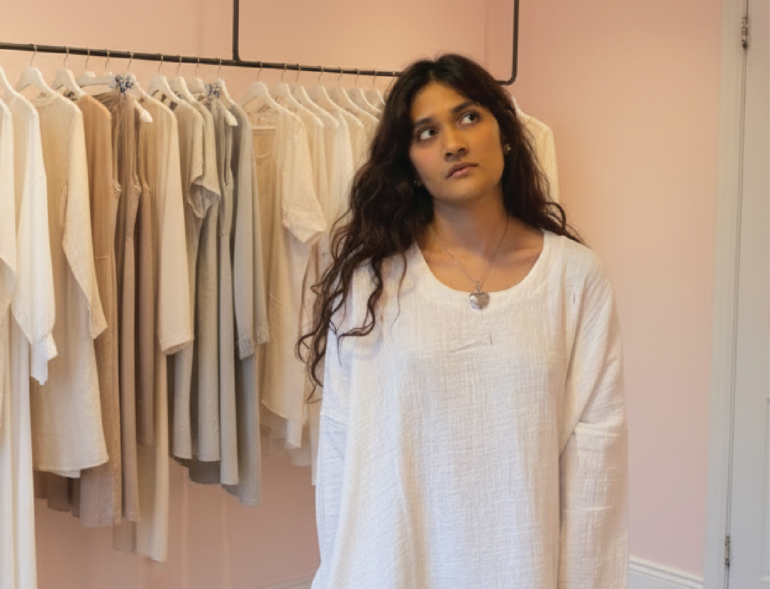 Woman standing in a room with racks of clothes and a mirror on the wall.