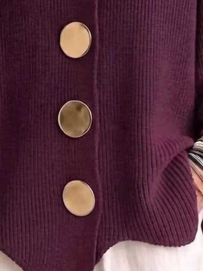 Close-up of a ribbed knit cardigan in deep plum purple with three large round metallic buttons, shown on a person wearing a white top.