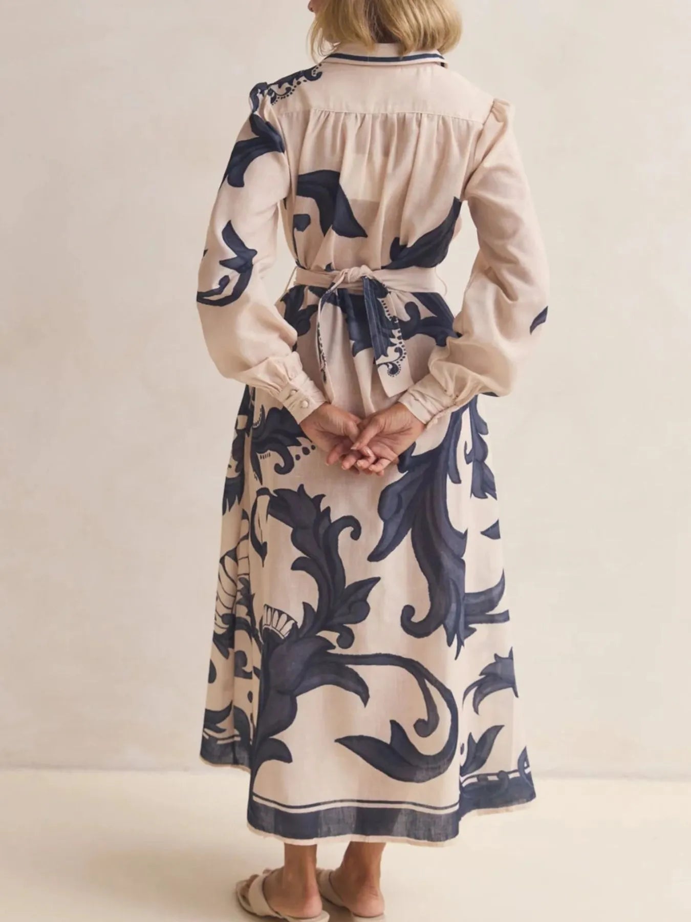 Person wearing a long dress with blue floral patterns on a plain background