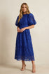 A woman modeling a royal blue lace midi dress with puff sleeves and a fitted waist, paired with nude high-heeled sandals against a plain light background.