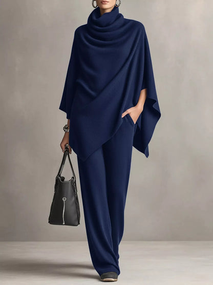 Person wearing a navy blue poncho and holding a black handbag against a neutral background