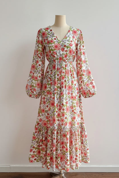 Floral dress on a mannequin against a plain wall with a vase of flowers on a table.