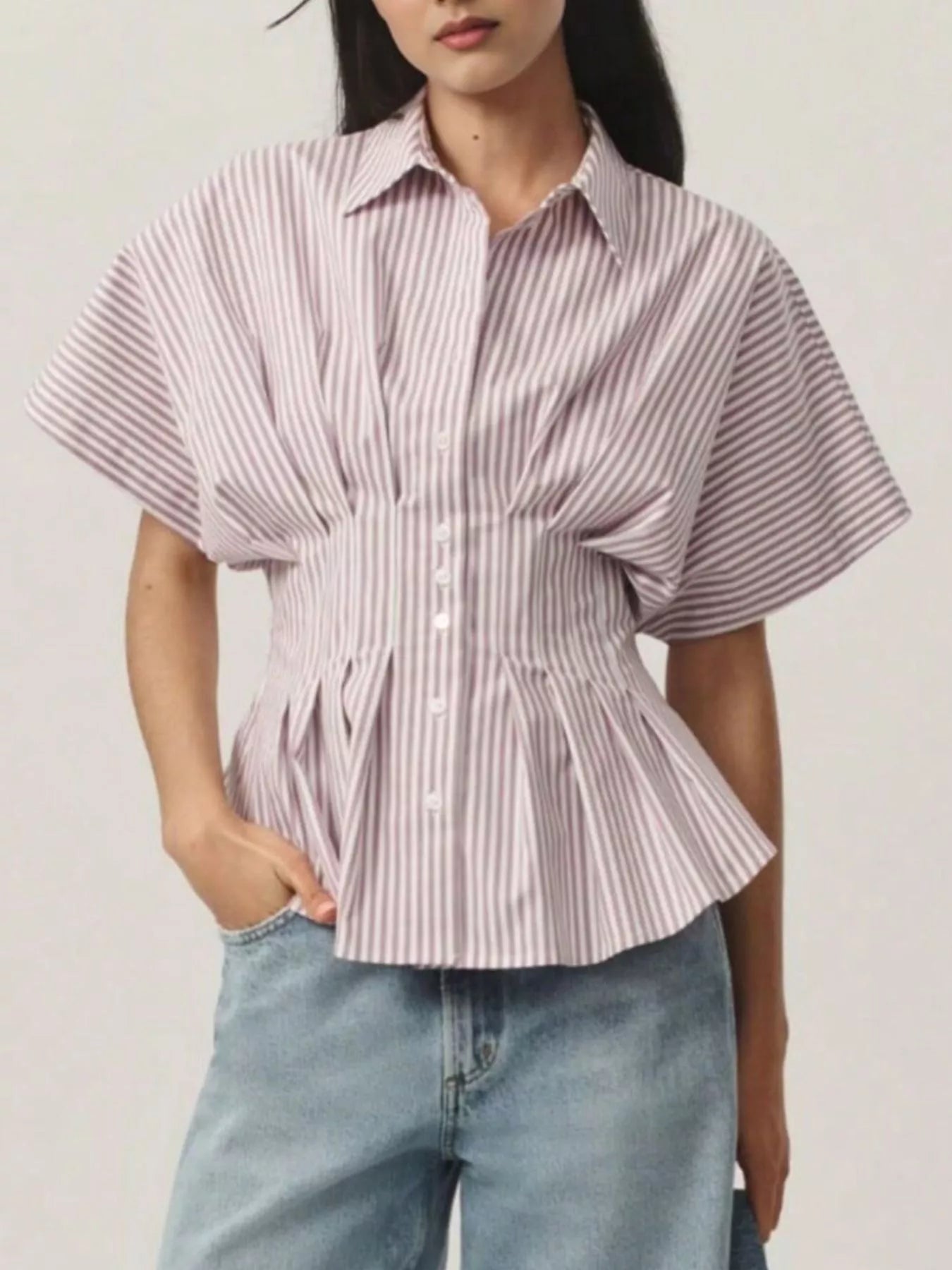 Person wearing a striped shirt with a peplum waist and light blue jeans on a plain background