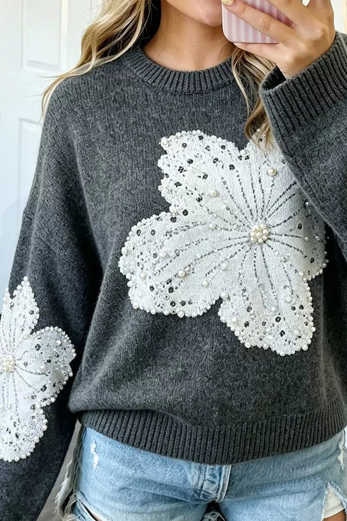 A woman wearing a dark gray knit sweater with large white floral lace appliques on the front and sleeves, paired with light blue denim shorts, shown in a mirror selfie.