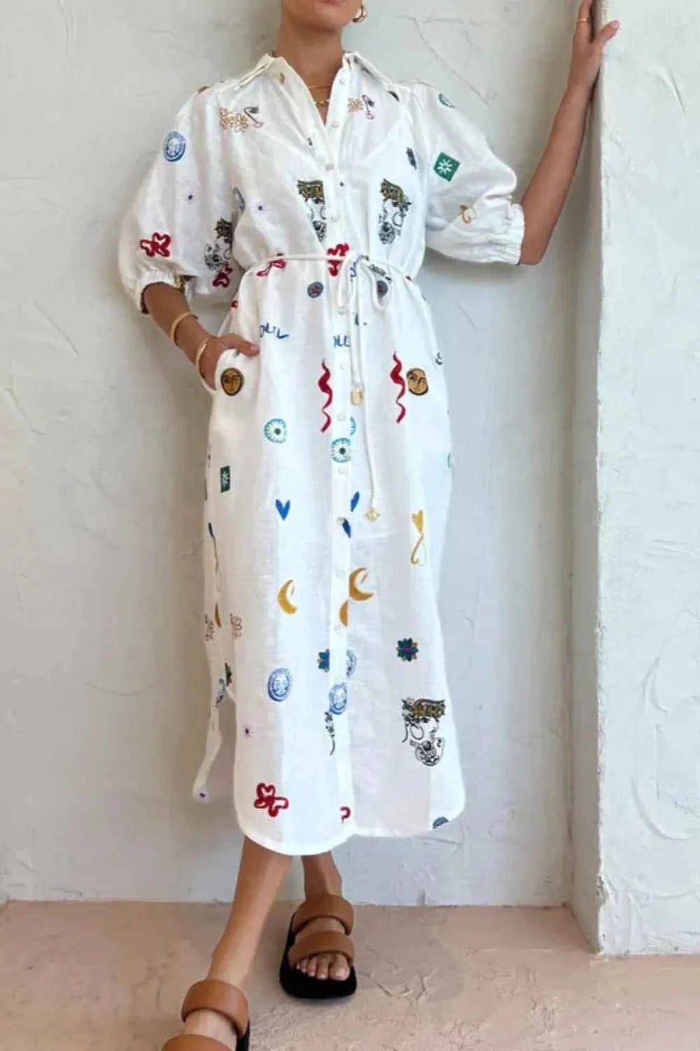 Person wearing a white dress with colorful patterns against a plain background