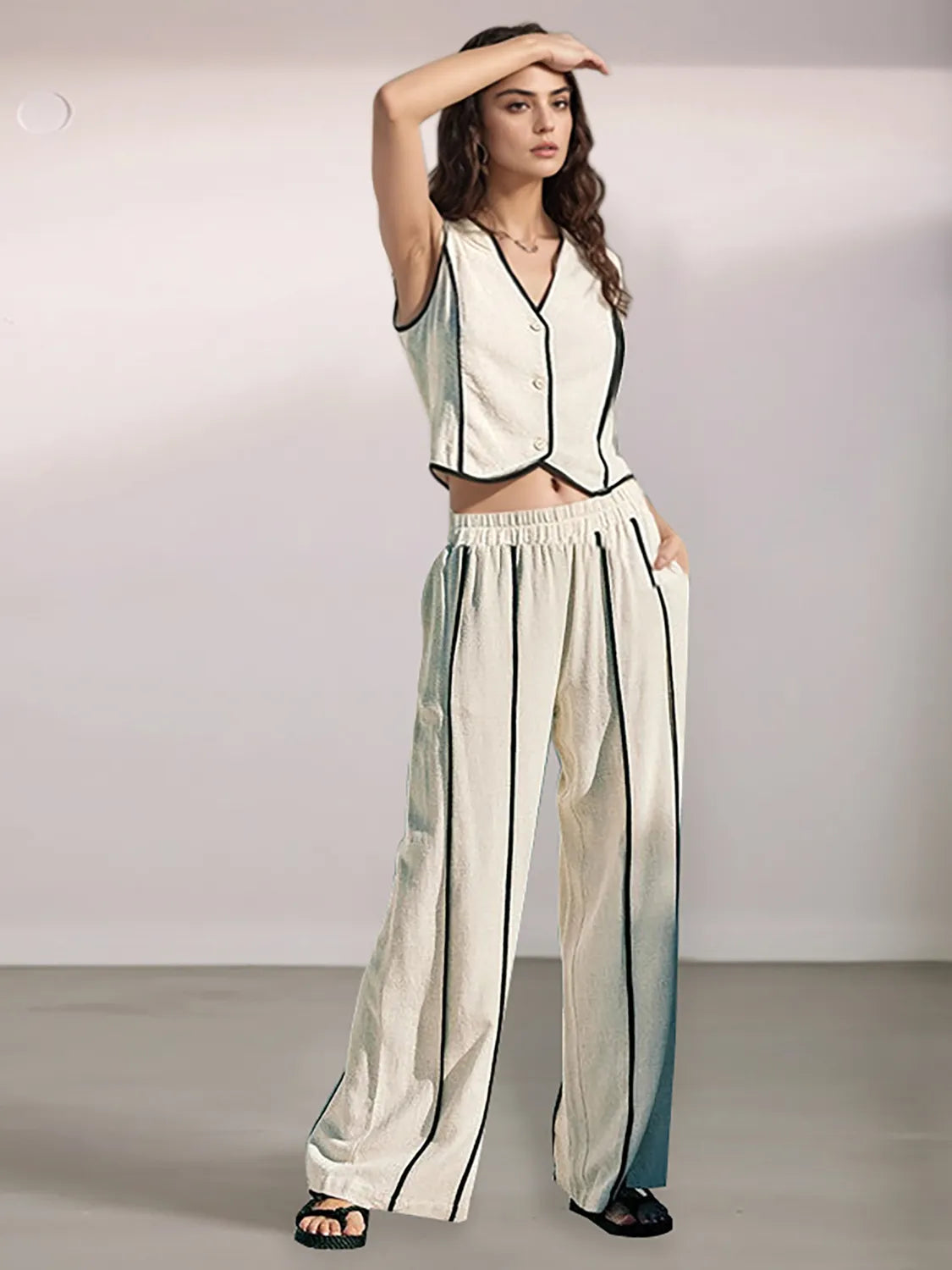 Woman wearing a white sleeveless top and wide-leg pants with black stripes on a plain background