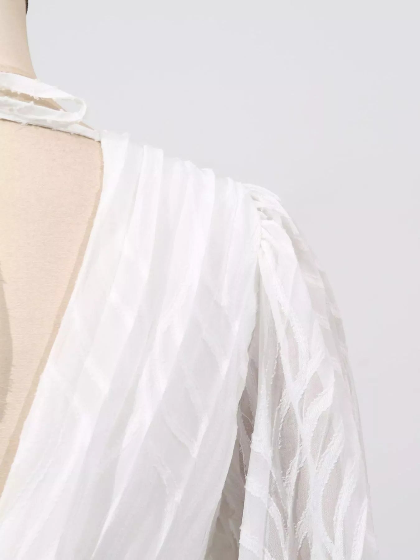 White dress with a sheer overlay on a mannequin against a light gray background