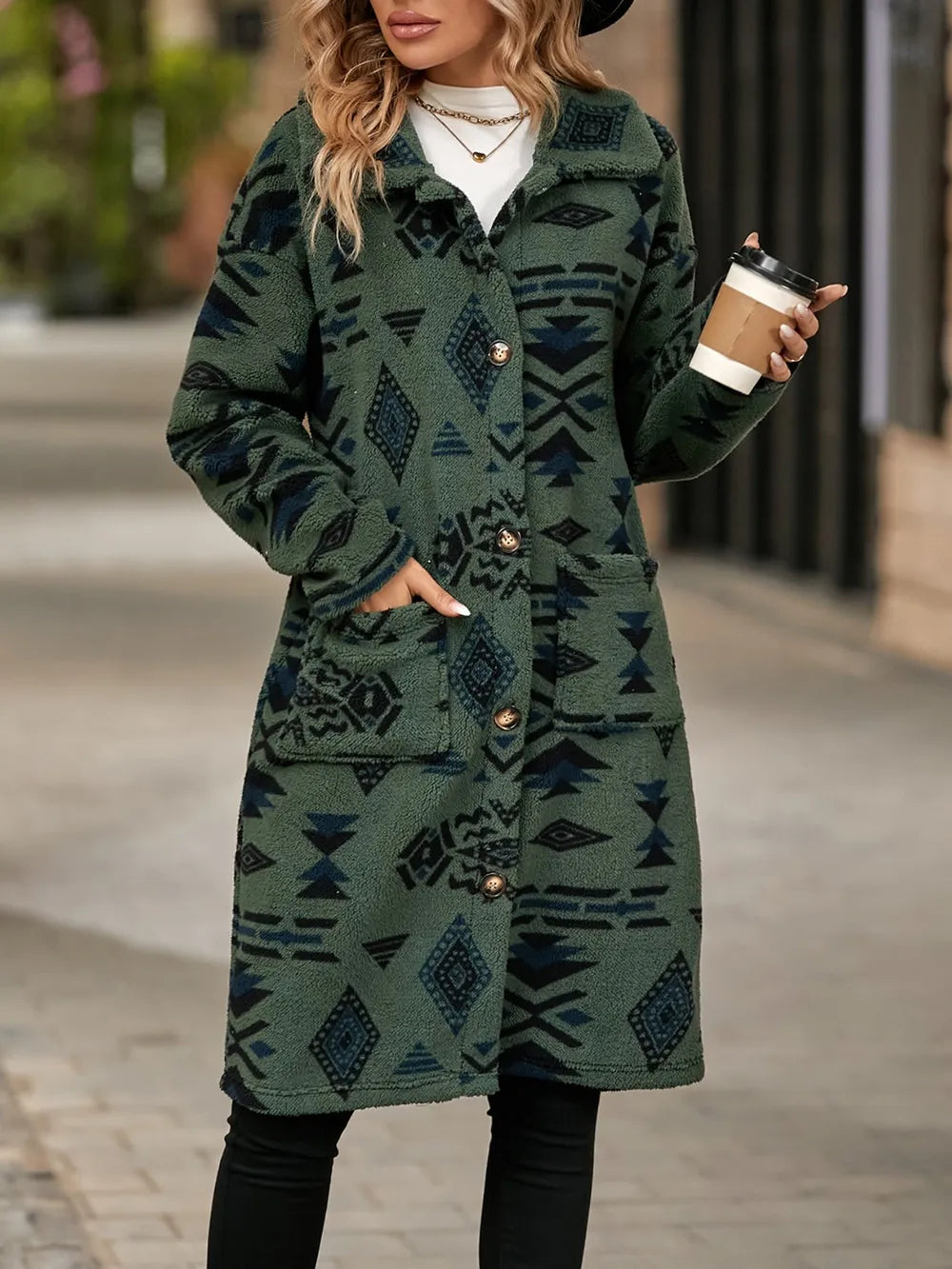 Woman wearing a green patterned coat holding a coffee cup on a street.