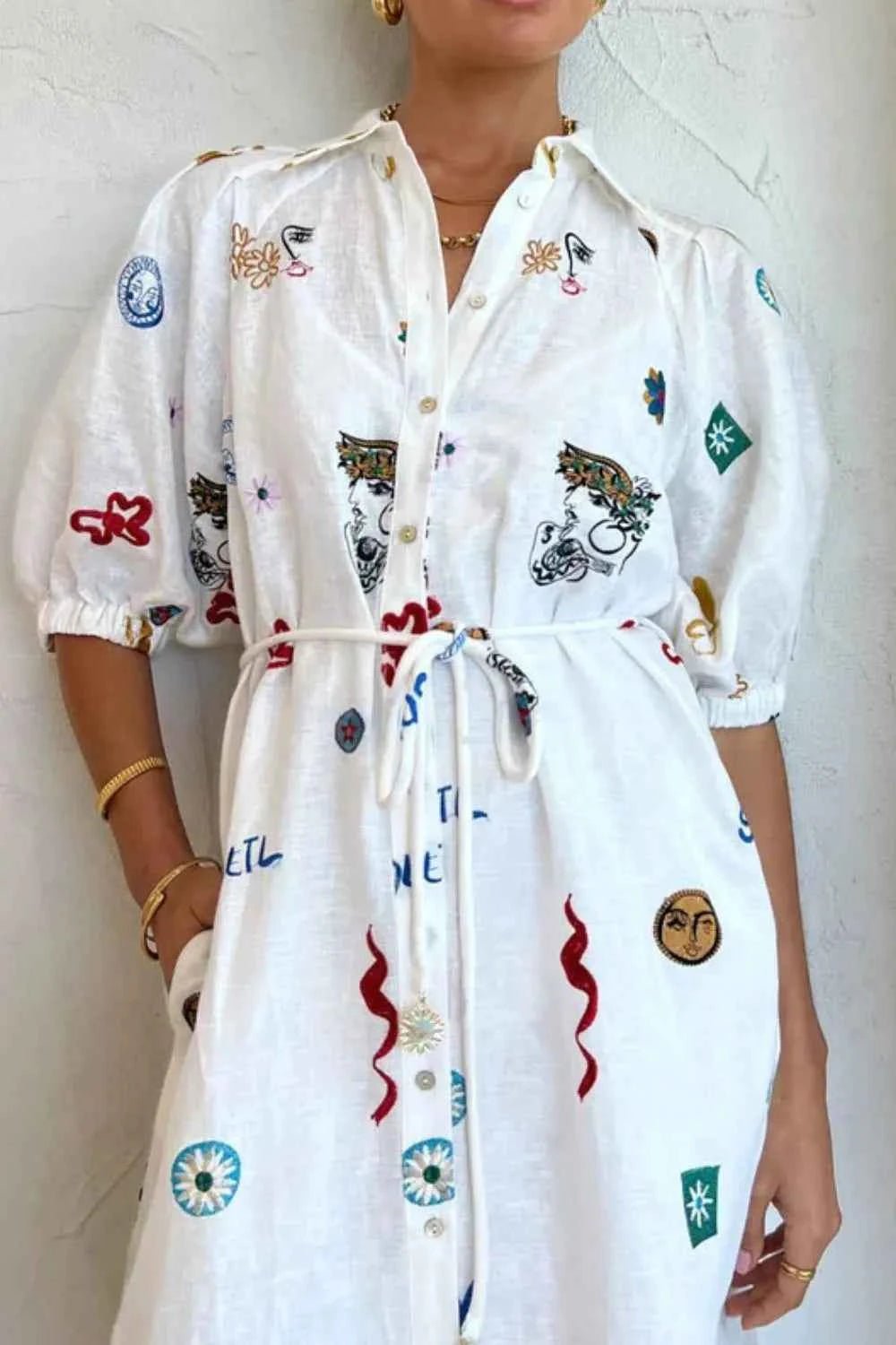 White dress with colorful patterns worn by a person against a white wall.