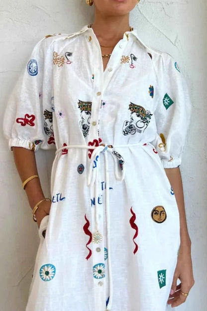 White dress with colorful patterns worn by a person against a white wall.