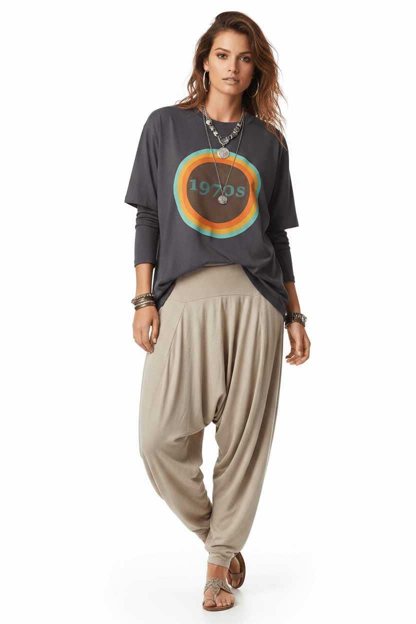 Woman wearing a dark gray t-shirt with a colorful graphic and beige harem pants on a white background